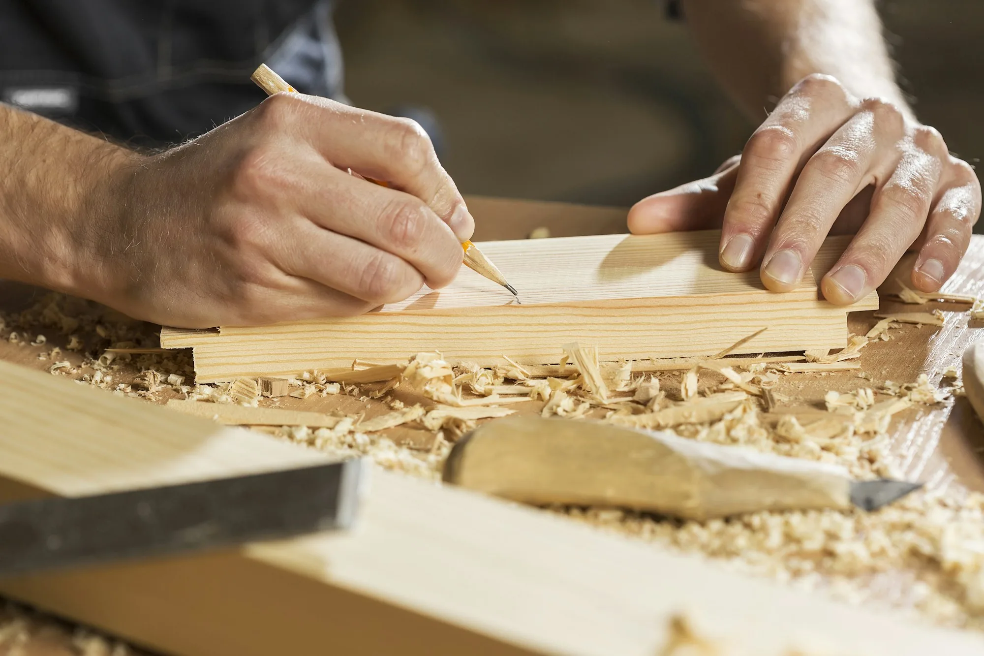 A carpenter's hands marking a length of timber at a bench